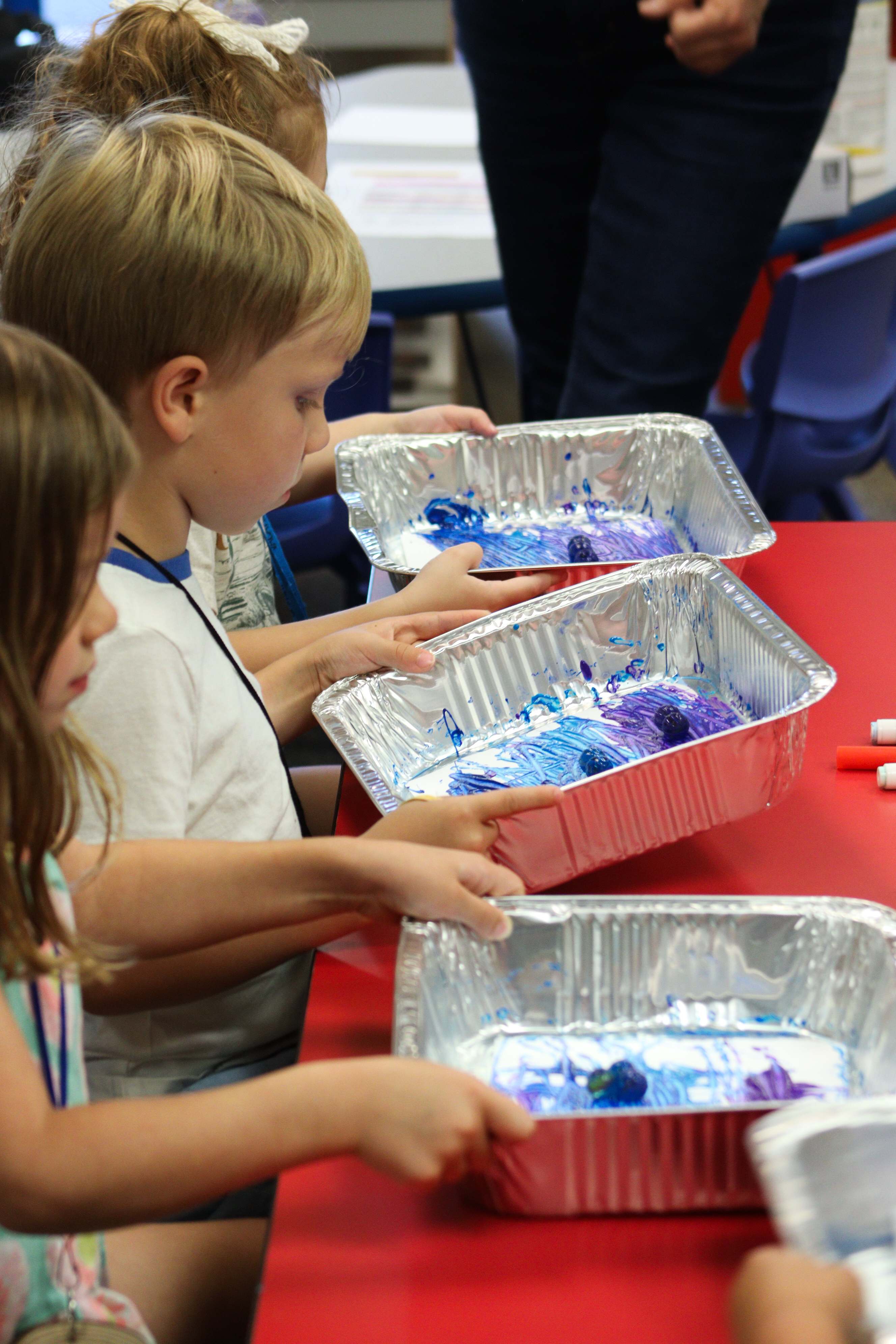 Three young kids rolling marbles in purple and blue paint