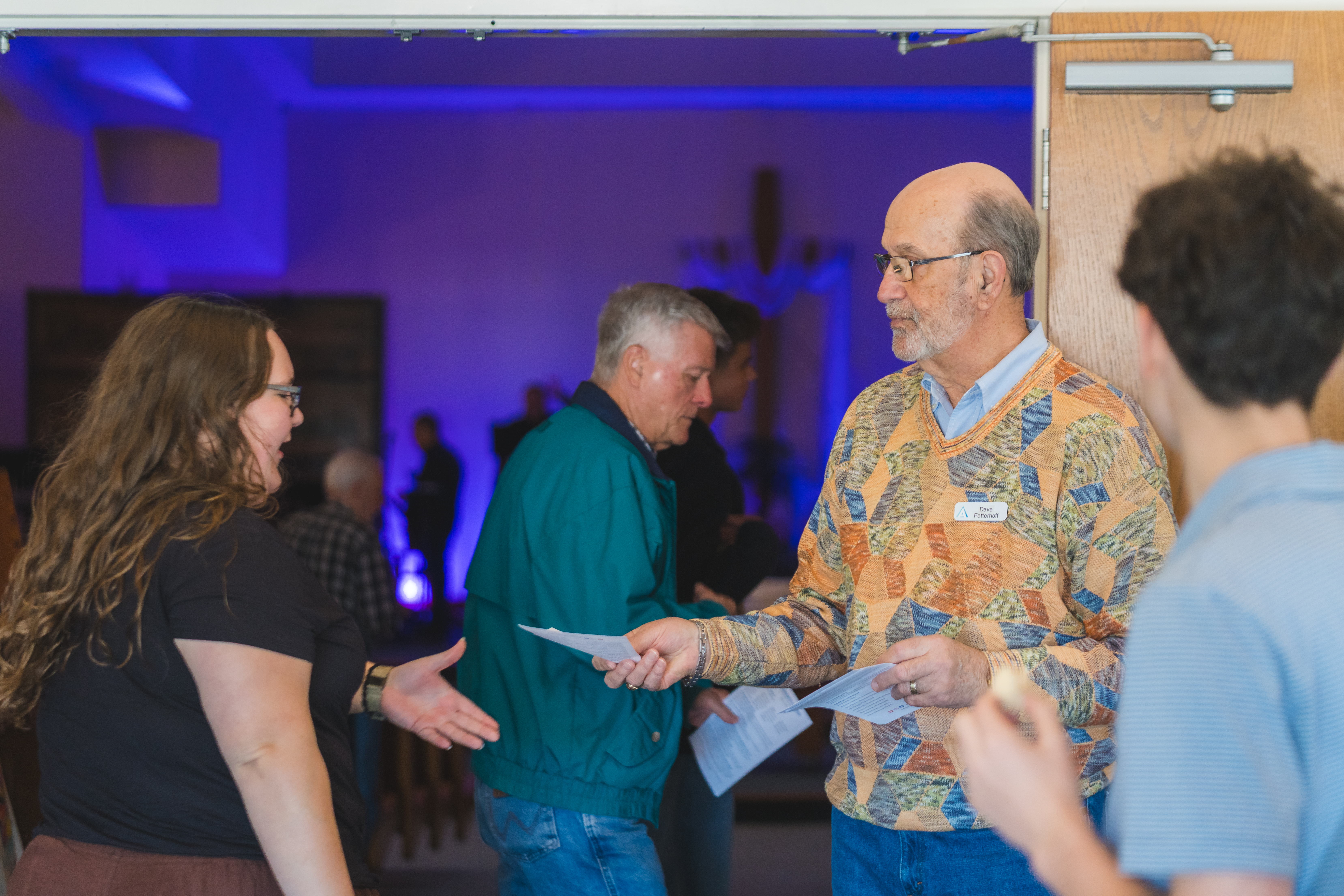 man handing a worship handout to a woman by the sanctuary doors