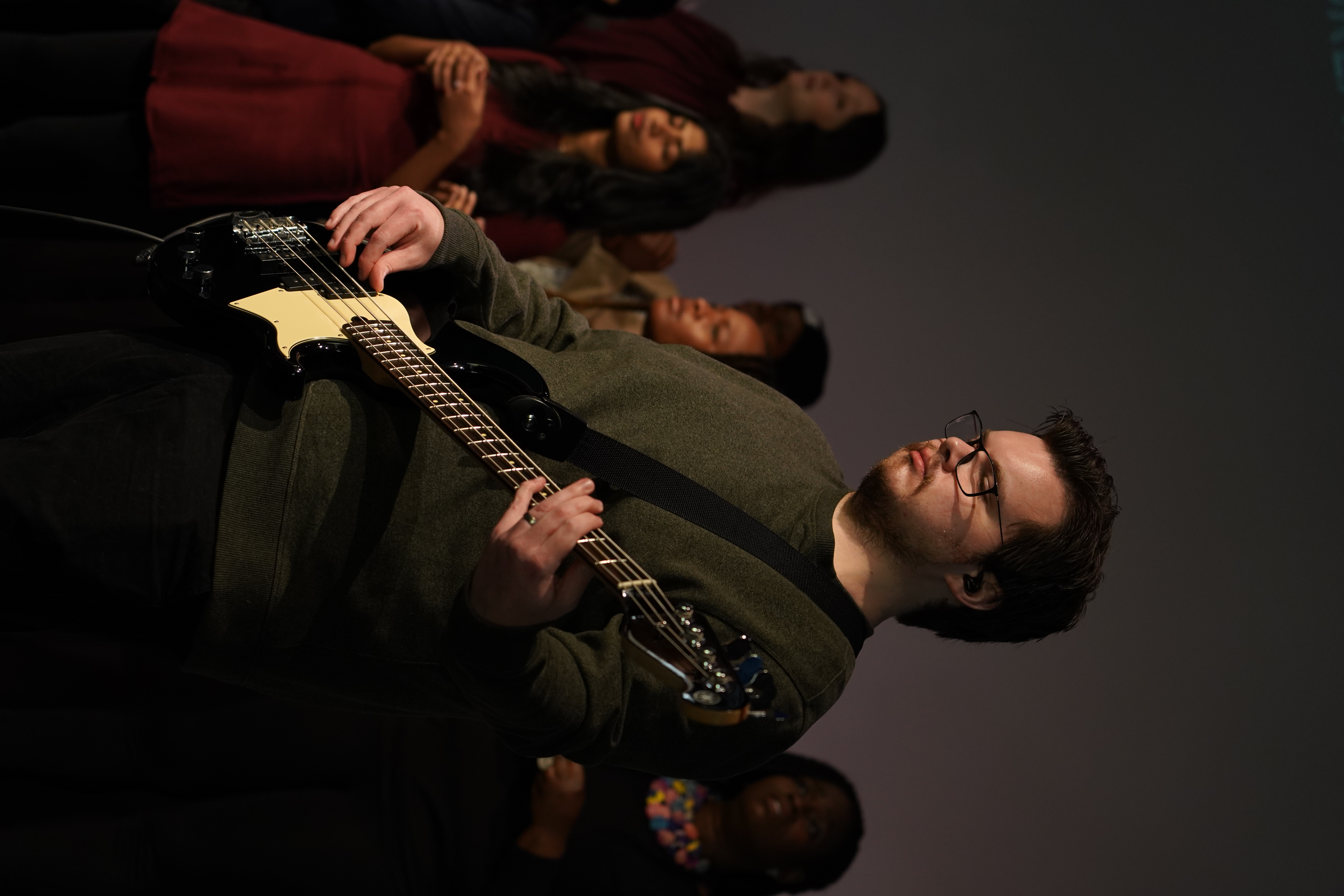 A musician playing bass on stage during a service at Faith Summit St, with the choir in the background.