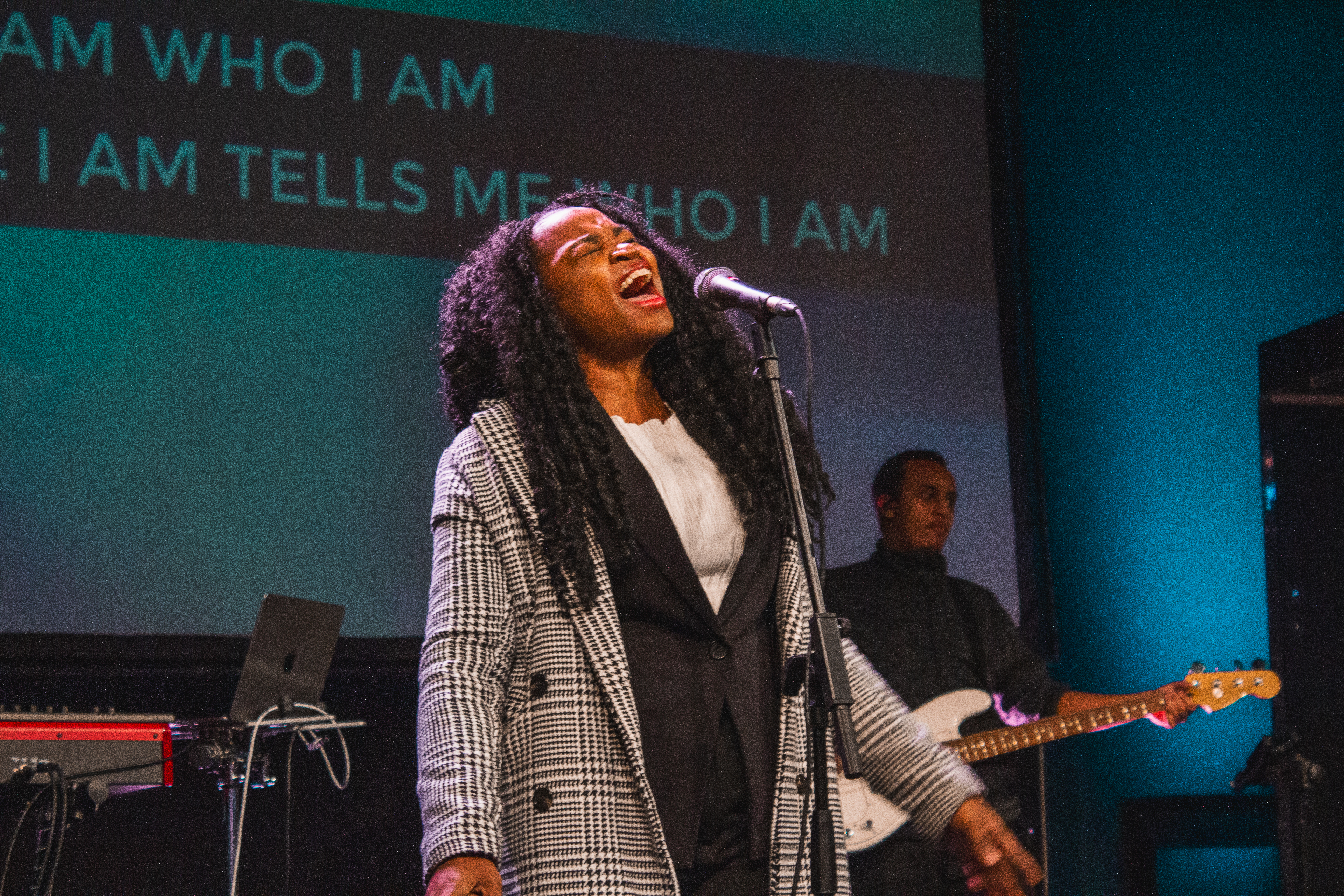 A singer leading worship on stage at Faith Summit St, passionately singing with the band and lyrics displayed behind.
