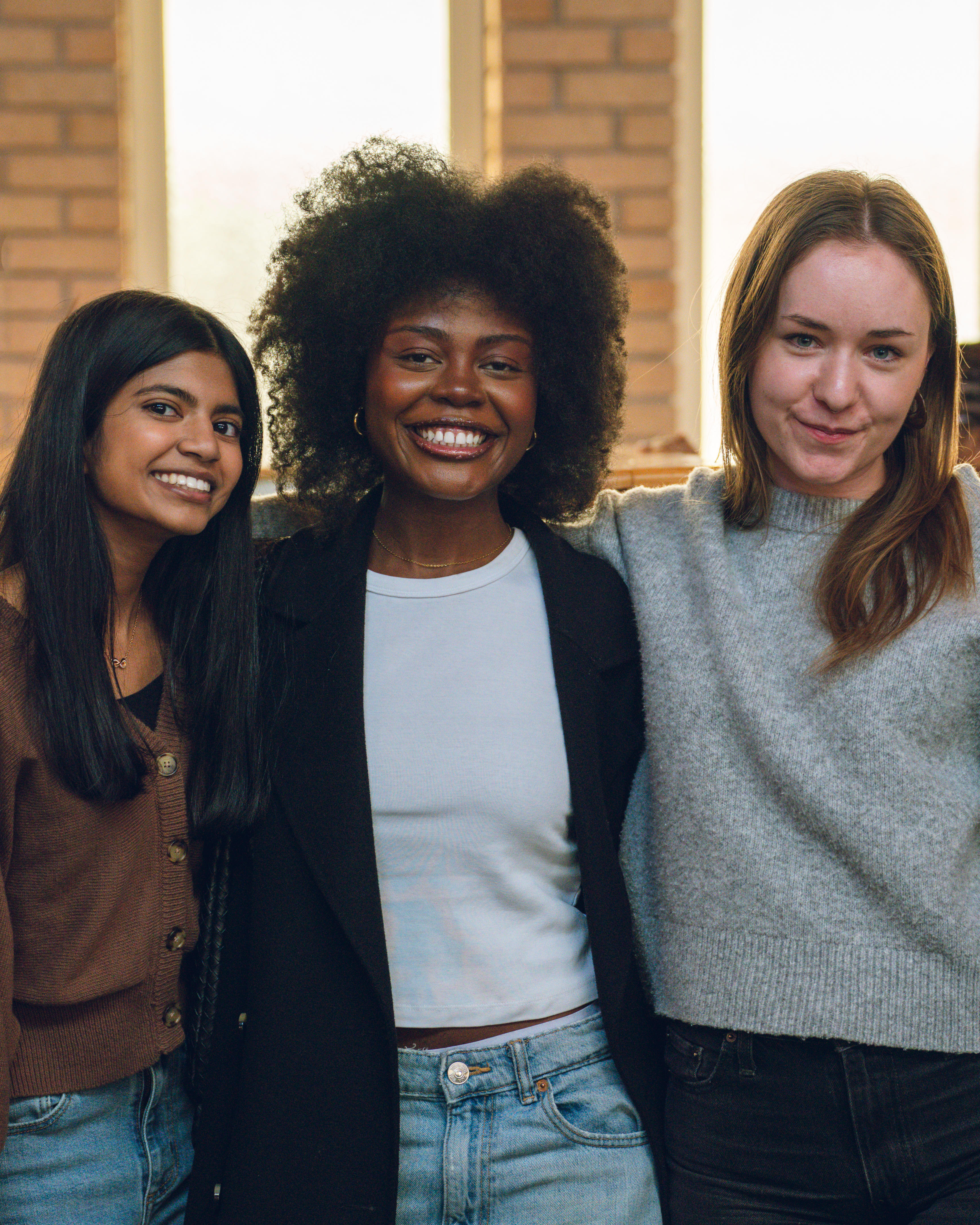 Three women smiling together inside Faith Summit St, standing in a bright, welcoming church space.