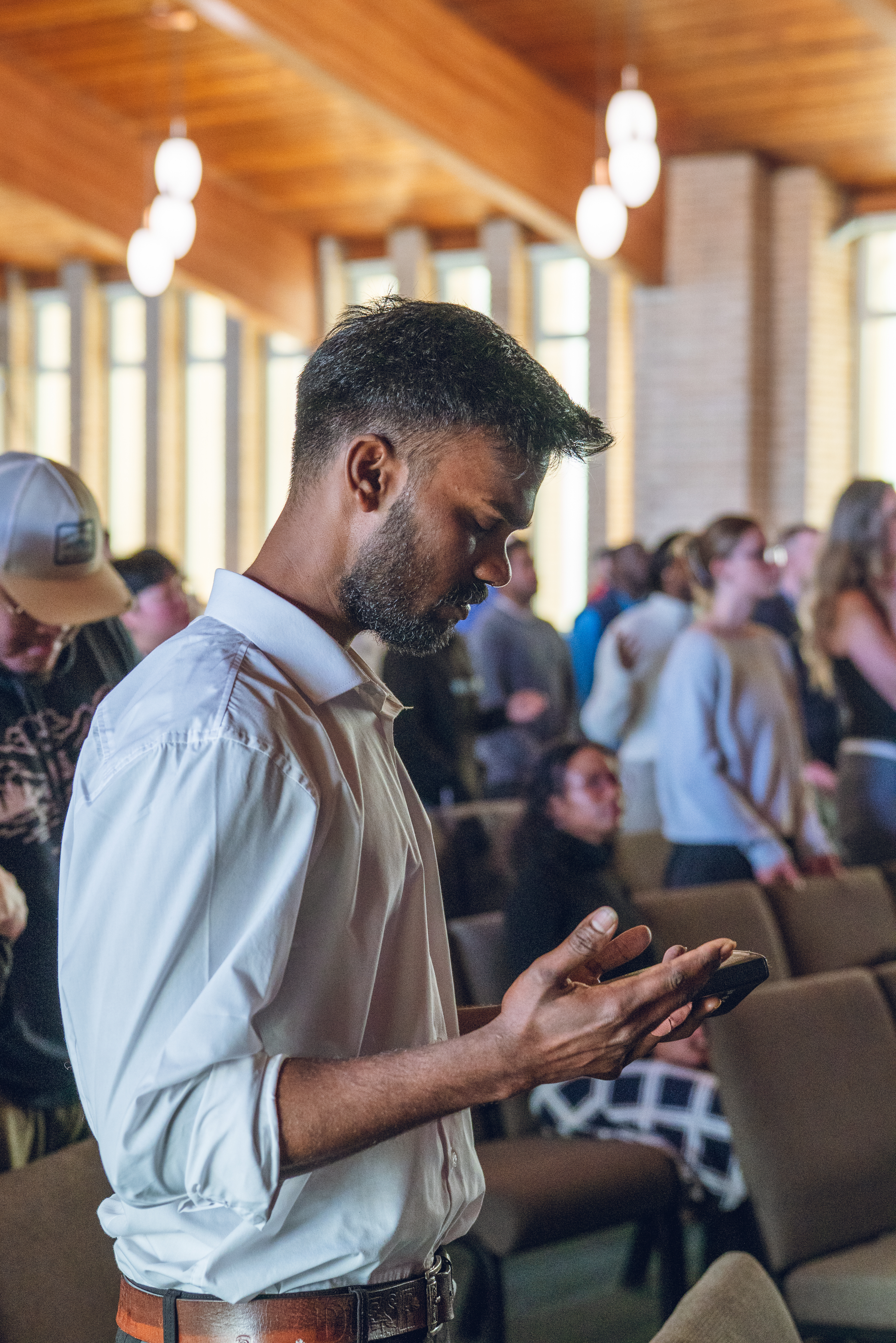 A man in fervent prayer in the Faith Summit St sanctuary, with a gathering of people in the background.