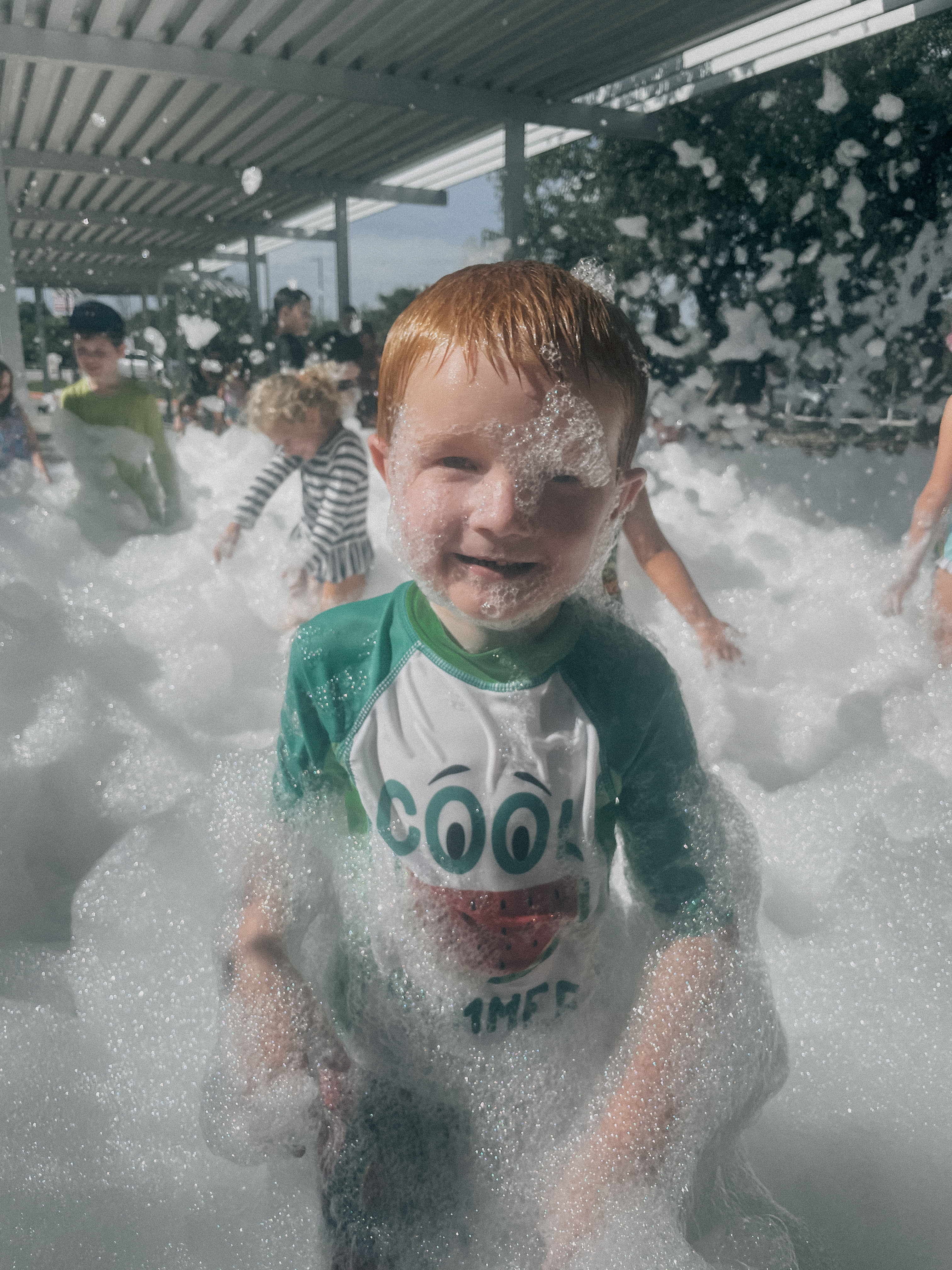 Smiling young boy covered in bubbles playing outside.