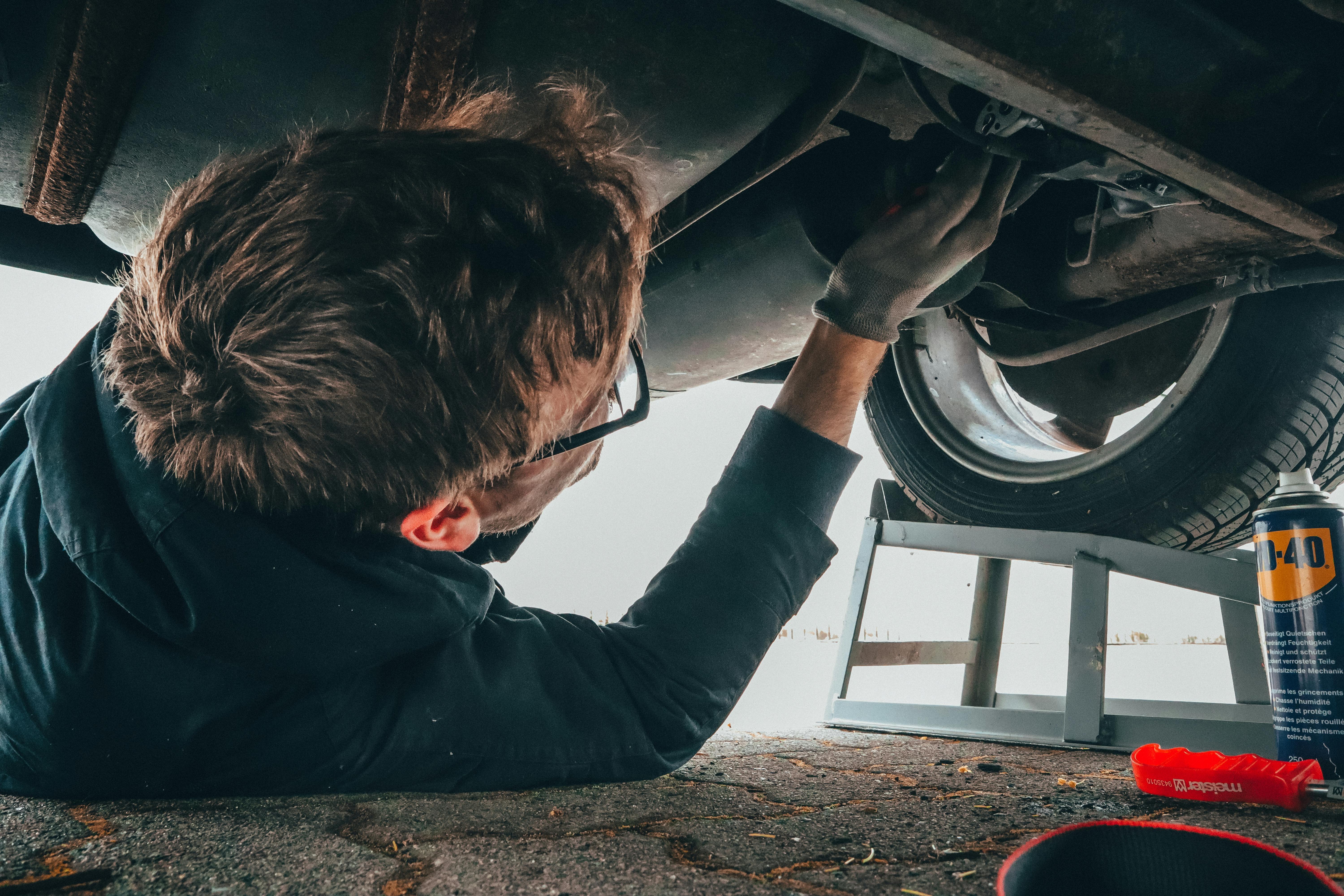 A mechanic lays on the ground beneath a car to change its oil.